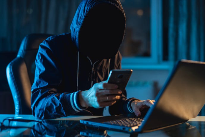 cybercrime concept showing shadowy hacker hacking a system in the dark