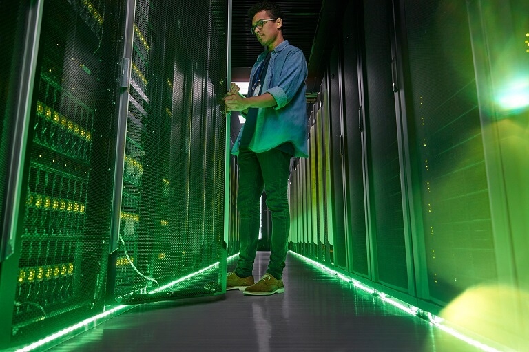 Male IT technician working in dark server room with glowing green panels