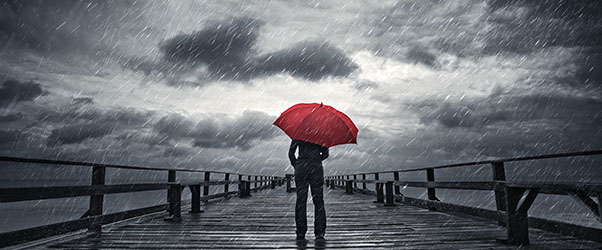 A person standing outside under gray rain clouds holding a red umbrella