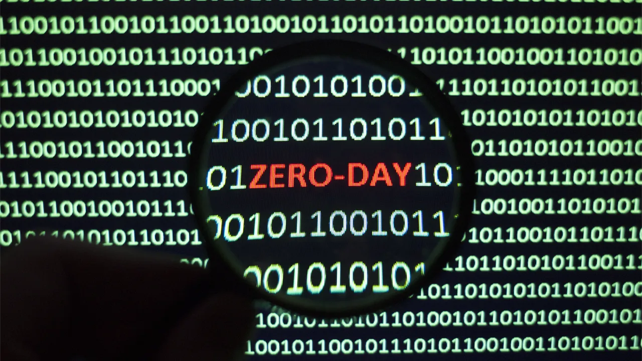 An IT professional holds a magnifying glass over a screen to illuminate the words 'zero-day' An IT professional holds a magnifying glass over a screen to illuminate the words 'zero-day'