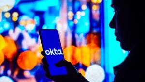 In this photo illustration, a silhouetted woman holds a smartphone with the Okta logo displayed on the screen.