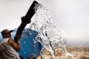 A Peruvian water distribution worker with a hose splashes drinking water from a truck in Pachacútec, Lima, Peru.