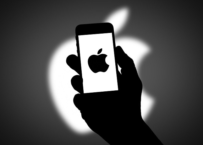 Mysterious figure holding Apple phone with shadowy background.