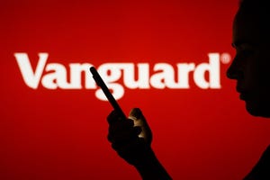 Vanguard Group logo is seen in the background of a silhouetted woman holding a mobile phone