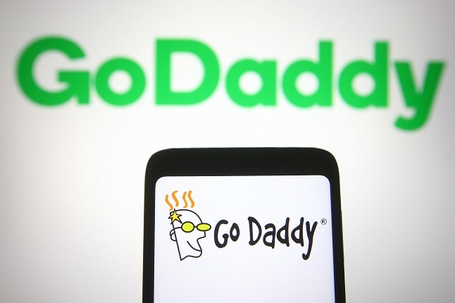 GoDaddy logo is seen on a smartphone and a pc screen.