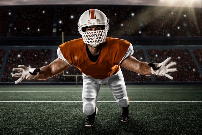 Football Player with a orange uniform making a tackle on a stadium.