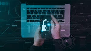 User at a keyboard holding a phone with a security icon User at a keyboard holding a phone with a security icon