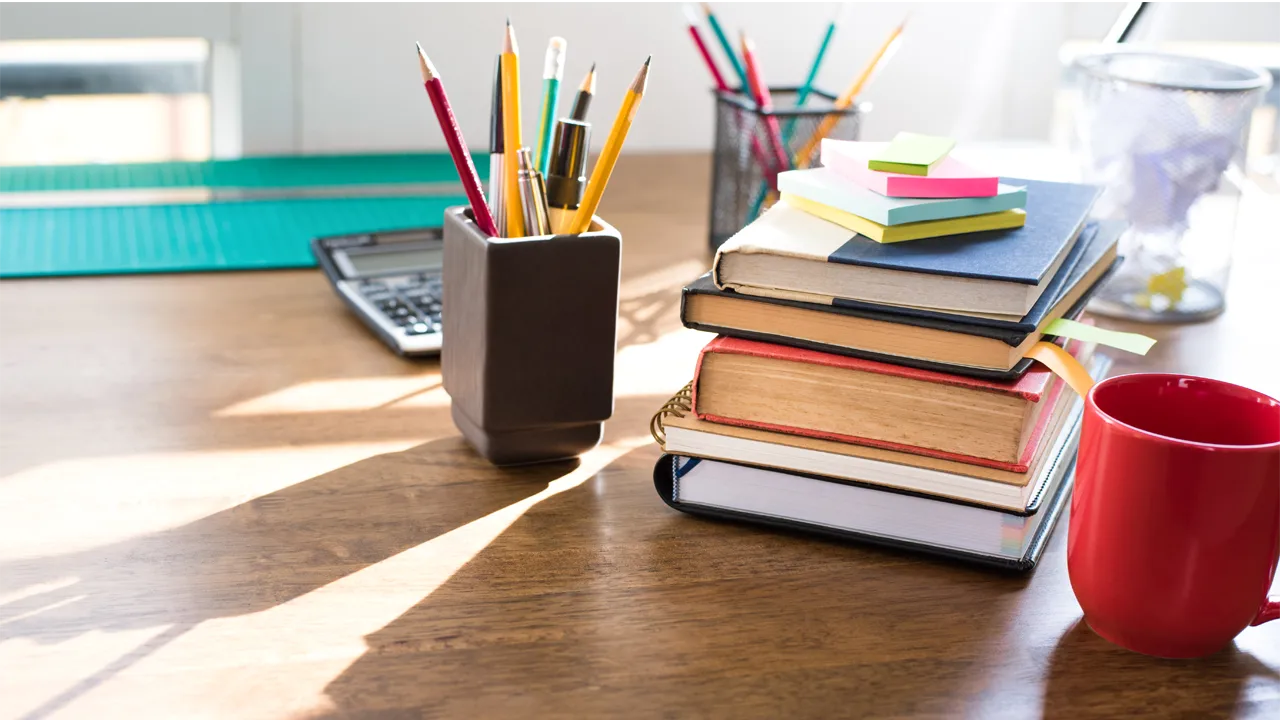 Books sit on a wooden table, with pencil cups and a calculator Books sit on a wooden table, with pencil cups and a calculator