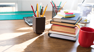 Books sit on a wooden table, with pencil cups and a calculator Books sit on a wooden table, with pencil cups and a calculator
