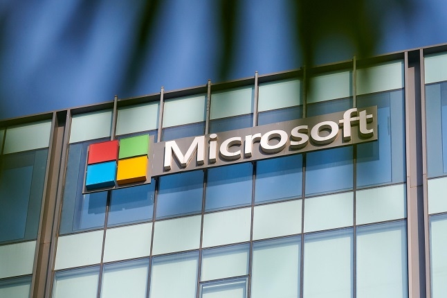 Microsoft corporation brand logo on high rise glass building exterior through exotic green palm leaves summertime photo.