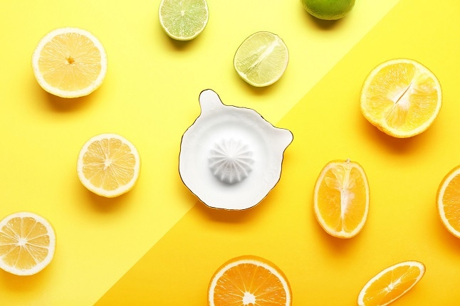 Ceramic juicer and citrus fruits on yellow background