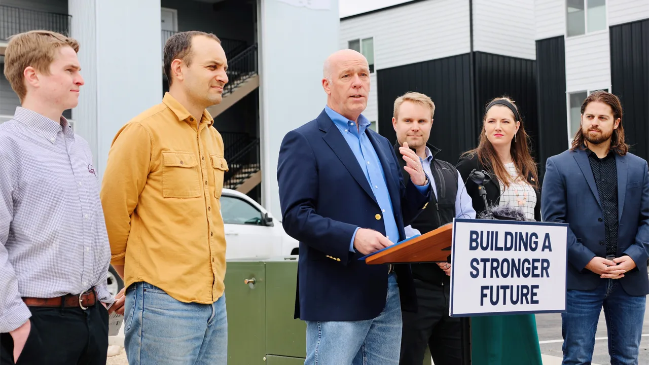Montana Governor Greg Gianforte stands in front of a podium with people on either side of him Montana Governor Greg Gianforte stands in front of a podium with people on either side of him