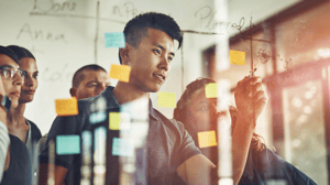 An IT team works together on a project at a transparent dry erase board An IT team works together on a project at a transparent dry erase board