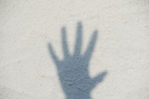 Shadow of a hand on a white wall. Five fingers. Stop.