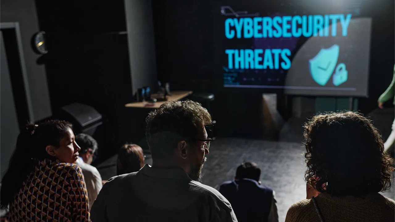 Attendees listen to a presentation at a cybersecurity conference. Attendees listen to a presentation at a cybersecurity conference.