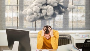 Cloud hovers over a man in distress due to his cloud service sitting at his work desk with his desktop and laptop open