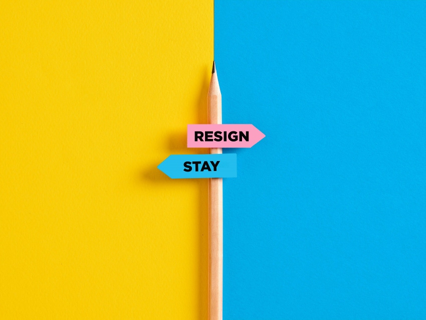 The dilemma between to resign or to stay at job concept. Pencil with direction indicator stickers showing the opposite words resign and stay.