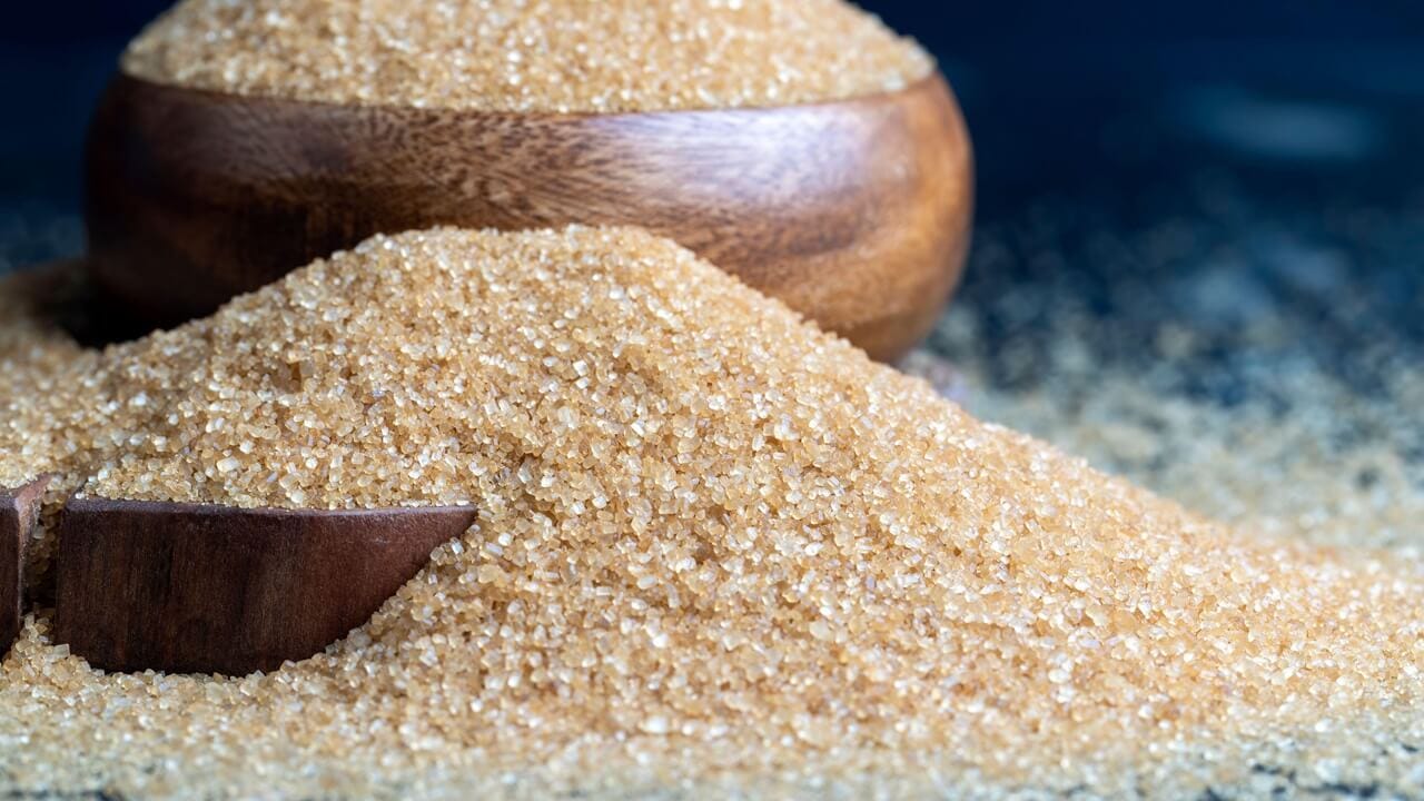 Brown crystalline sugar from cane, poured into a bowl and on the table sugar from brown cane Brown crystalline sugar from cane, poured into a bowl and on the table sugar from brown cane
