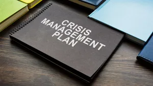 A notebook labeled 'crisis management plan' sits on a desk. A notebook labeled 'crisis management plan' sits on a desk.