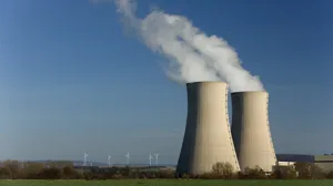 Two steaming cooling towers and a wind turbine farm Two steaming cooling towers and a wind turbine farm