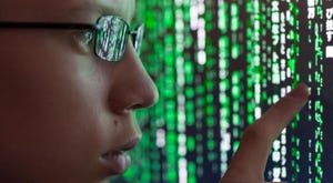A young man with glasses is watching futuristic symbols on a computer screen. Symbols are reflecting in the man's glasses.
