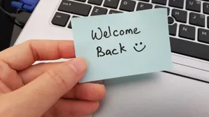An executive holds a sticky reading 'Welcome back,' with a smiley face An executive holds a sticky reading 'Welcome back,' with a smiley face
