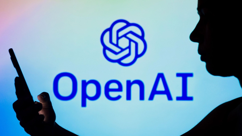 In this photo illustration, the OpenAI logo is seen in the background of a silhouetted woman holding a mobile phone
