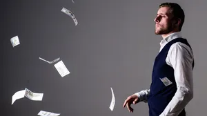 Man with strict face wasting money. Banknotes, cash dollars fly in air around. Man in formal wear, businessman throwing money on grey background. Man with strict face wasting money. Banknotes, cash dollars fly in air around. Man in formal wear, businessman throwing money on grey background.