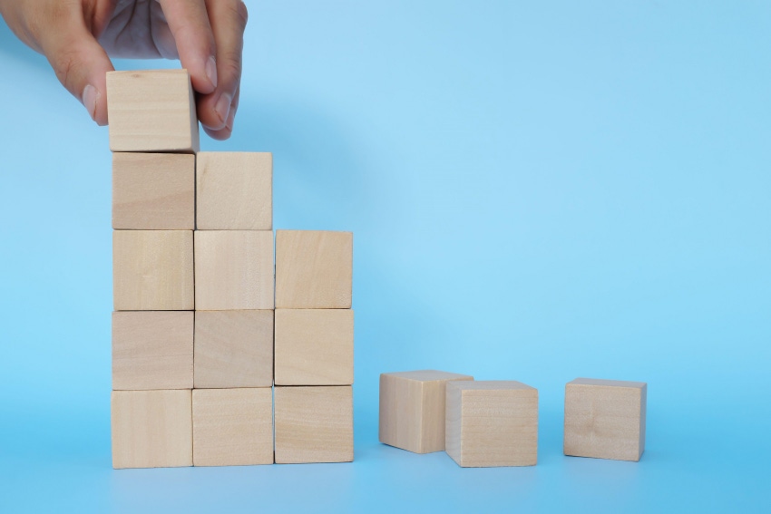 Hand putting together broken or fallen building blocks in blue background. rebuilding concept.