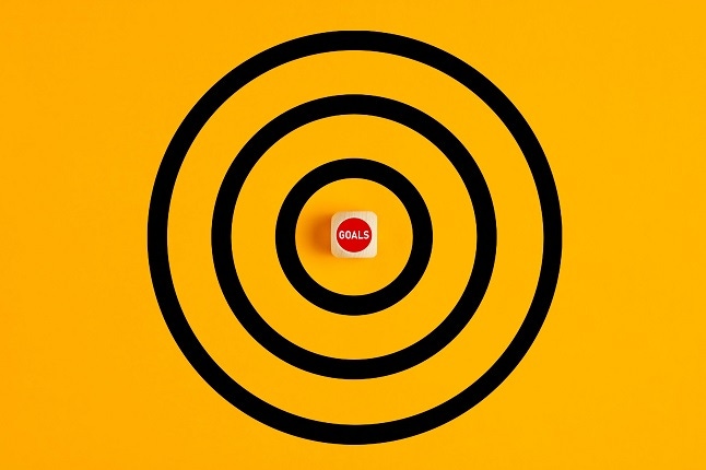 Target with the word goals written on a wooden block as the bulls eye on yellow background. Concept of achieving goals