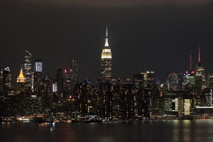 A nighttime view of Manhattan with illuminated skyscrapers and the East River in the foreground, as seen from Brooklyn.