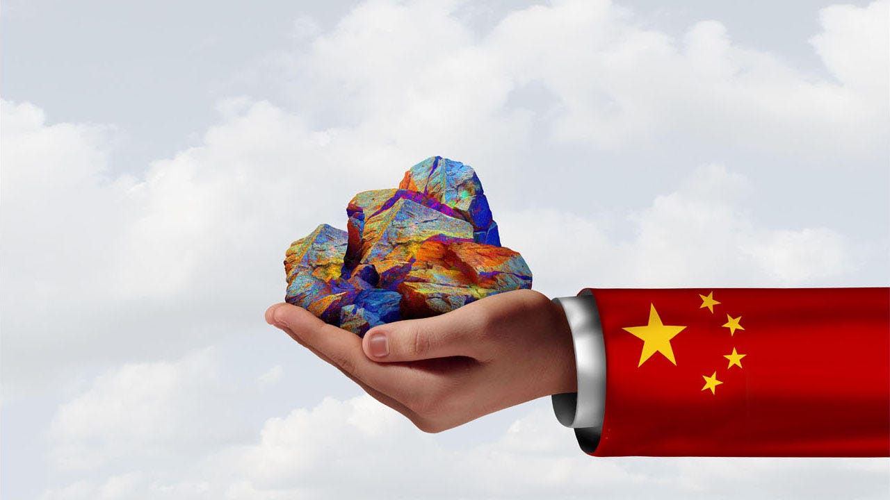 A person wearing a suit jacket in a Chinese flag design reaches out with a rare earth mineral in hand. A person wearing a suit jacket in a Chinese flag design reaches out with a rare earth mineral in hand.