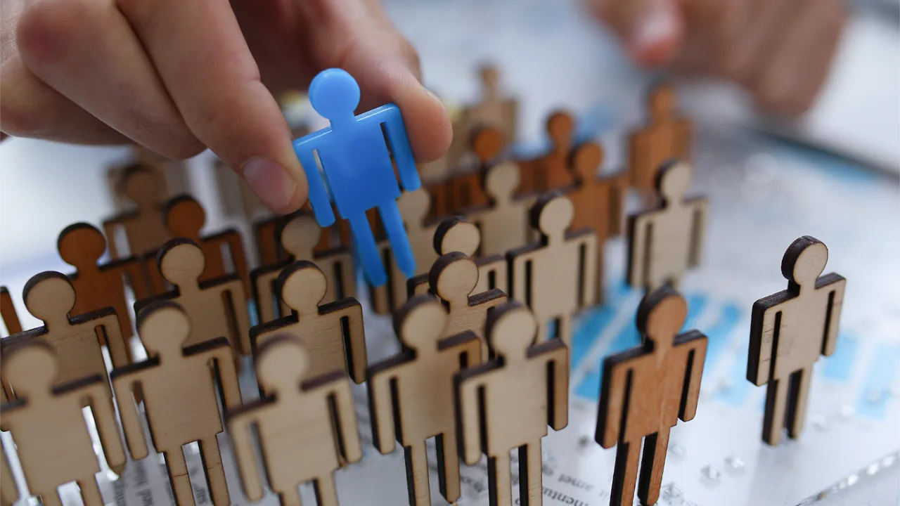 A businessman pulls a blue wooden figure of a person from a series of wooden figures A businessman pulls a blue wooden figure of a person from a series of wooden figures