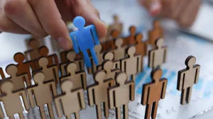 A businessman pulls a blue wooden figure of a person from a series of wooden figures A businessman pulls a blue wooden figure of a person from a series of wooden figures