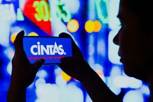 A silhouetted woman holds a smartphone with the Cintas Corporation logo displayed on the screen.