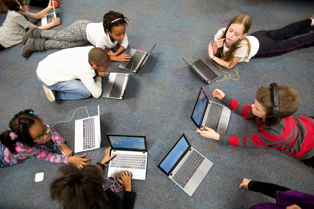 School children lying on the floor using laptops