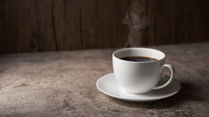 A cup of black coffee in a white mug sat atop a worktop in front of a wooden wall