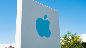 Close-up of blue logo on sign with facade of headquarters buildings in background near the headquarters of Apple Computers in the Silicon Valley