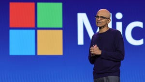 A bald man in a dark blue jumper stands in front of the Microsoft logo