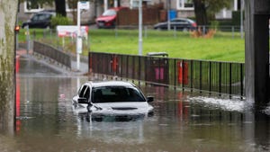 A car in a flooded street, its wheels and bottom half partially submerged