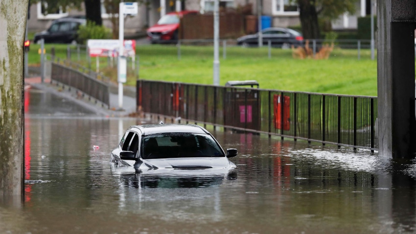 A car in a flooded street, its wheels and bottom half partially submerged