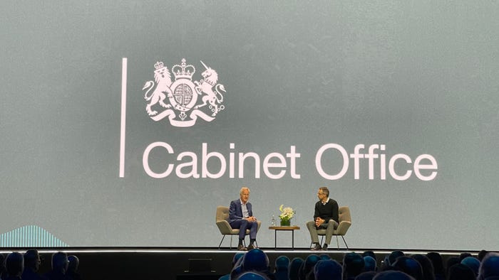 Two men talk on a stage in front of a grey background that reads 'Cabinet Office'