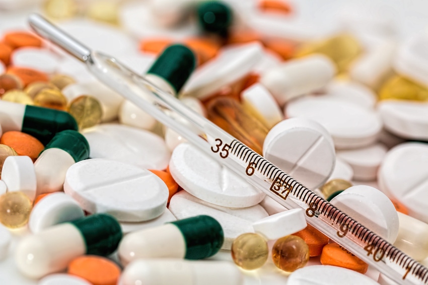 A stock image of a thermometer resting on a variety of medical pills 