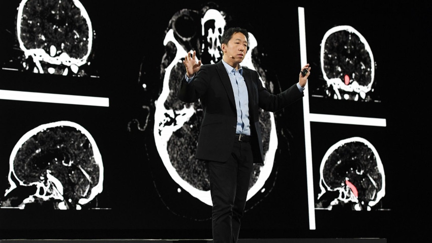 A man in a suit on stage, his arms in the air as he delivers a speech. He is standing in front of a dark background with a white outline of a brain