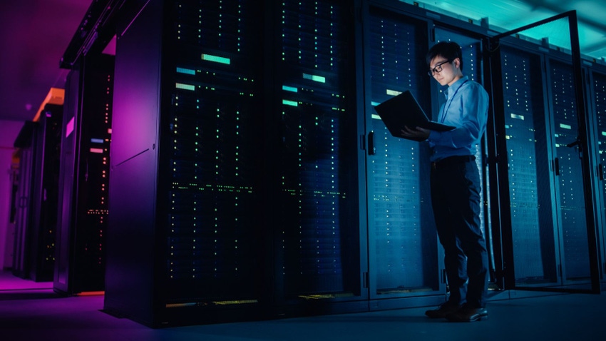 An engineer holding a laptop stands beside a infrastructure stack in a data center