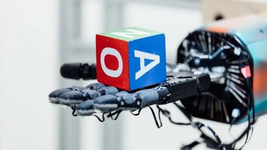 A robotic hand holding a cube with letters on it