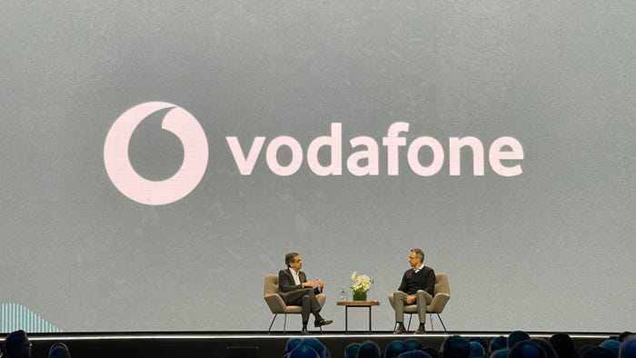 Two men talk on a stage in front of a grey background that reads 'Vodafone'