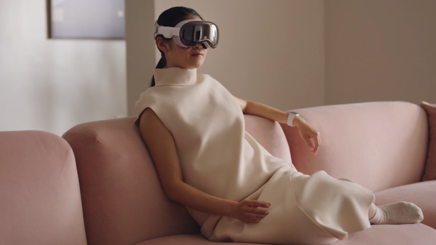 Woman wearing Apple's Vision Pro AR/VR headset on a couch