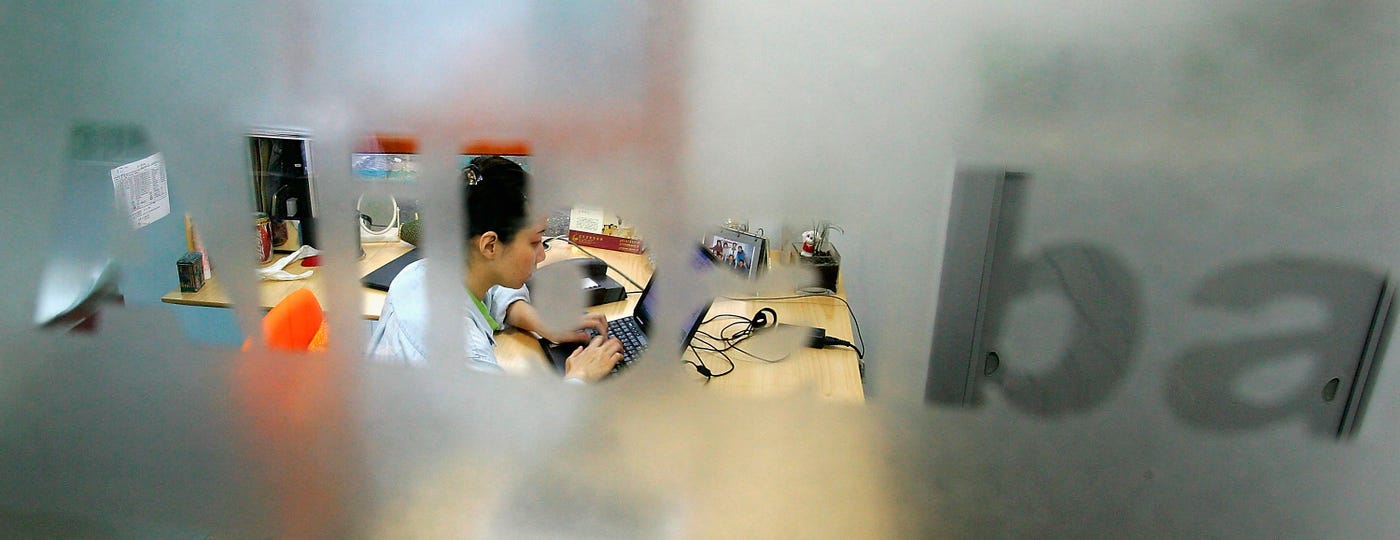 Woman working on laptop behind Alibaba logo Woman working on laptop behind Alibaba logo