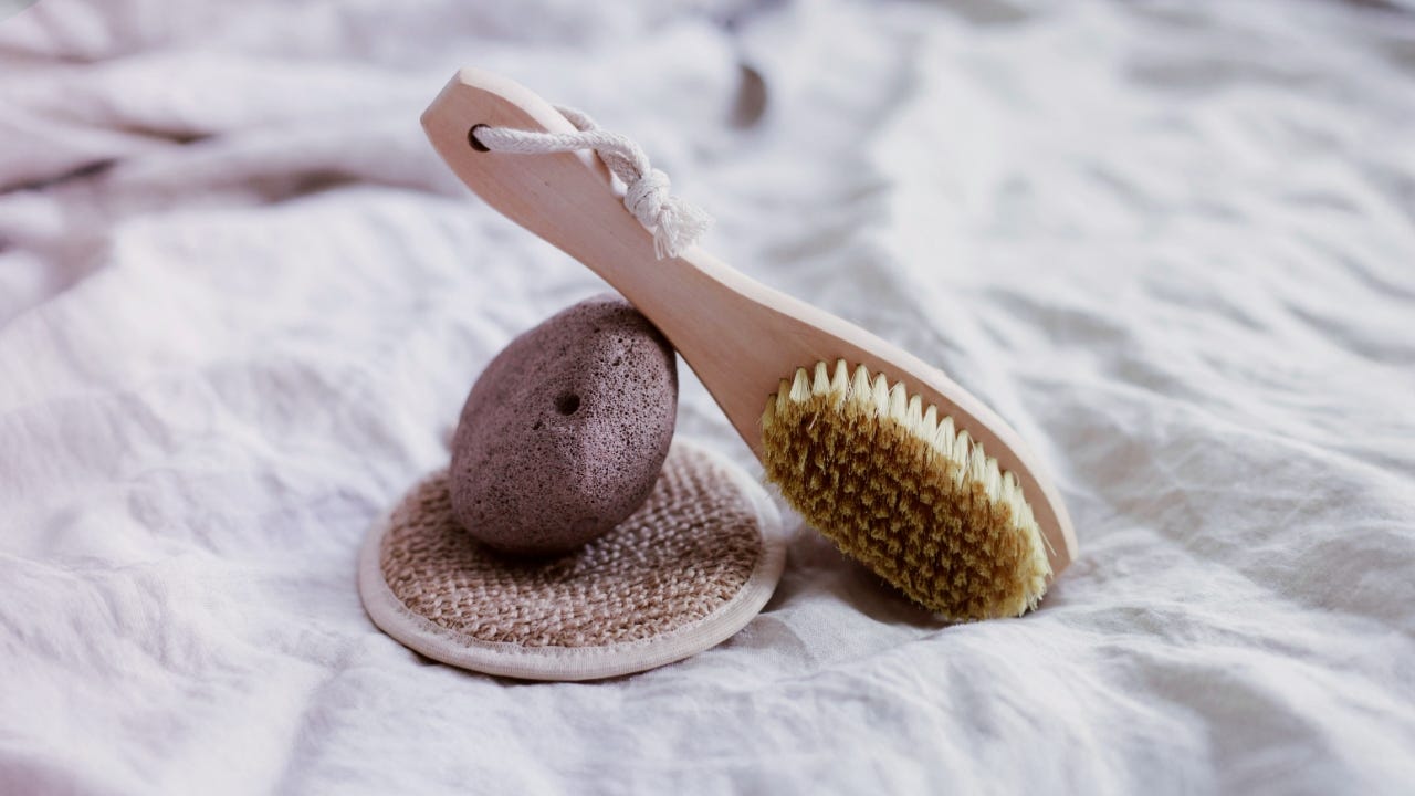 A close-up of a loofah, scrub brush, and exfoliation towel on a white surface.